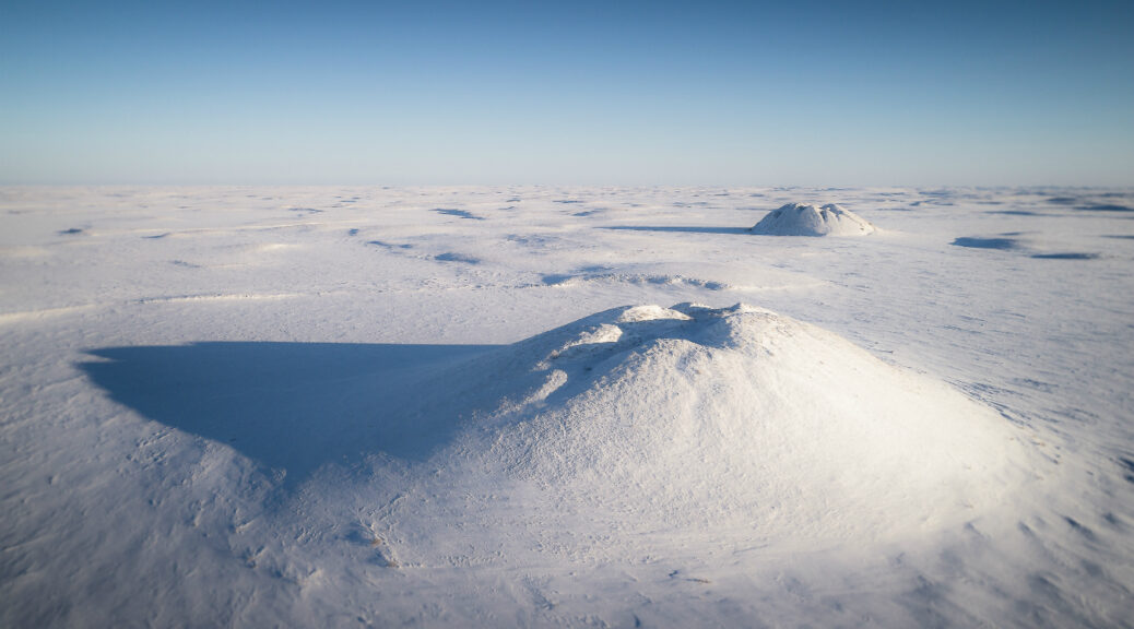 Ice-cored pingos emerge from permafrost and dot the arctic landscape near Tuktoyaktuk. Photo Credit: https://montecristomagazine.com/travel/northern-canada-ice-road